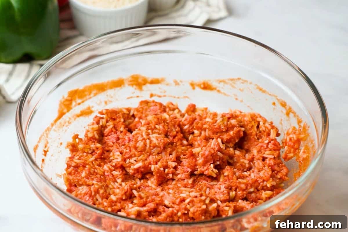 Mixing Stuffed Pepper Filling Ingredients A large mixing bowl filled with a savory blend of cooked rice, lean ground beef, rich tomato sauce, and a variety of aromatic seasonings, all mixed and ready for stuffing.