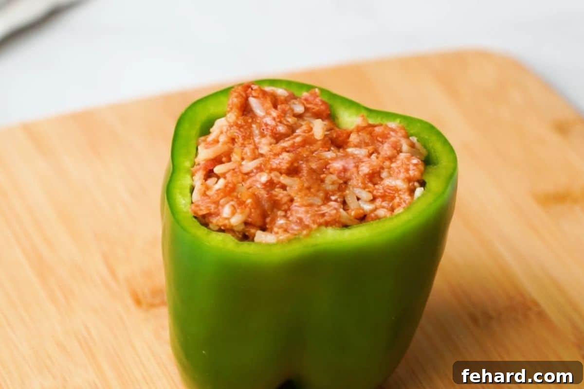Stuffed Bell Pepper Preparation A vibrant green bell pepper, perfectly hollowed and then generously stuffed with the savory rice and beef mixture, positioned on a cutting board, ready for cooking.