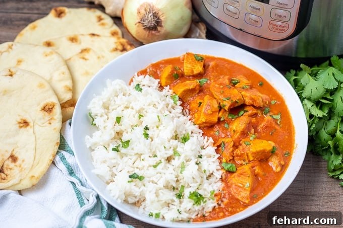 Butter Chicken Instant Pot A bowl of Instant Pot Butter Chicken served with Naan bread and the Instant Pot in the background.