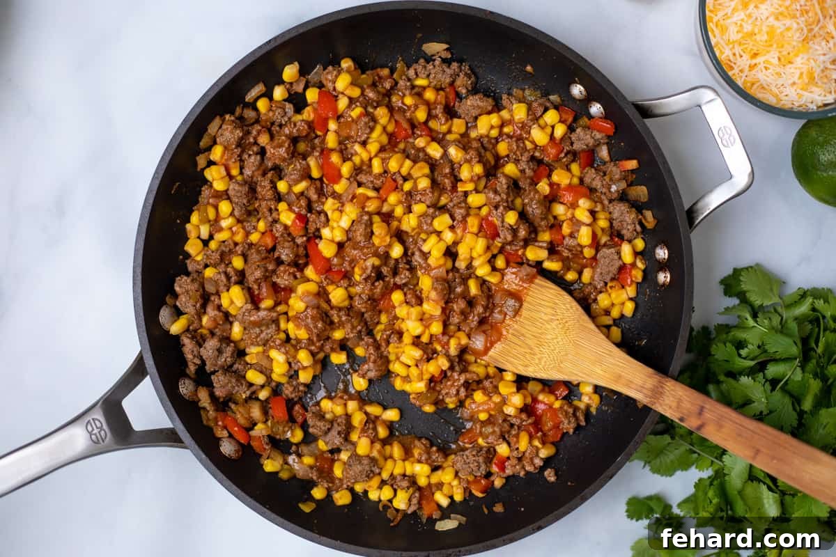 Close-up shot of a skillet filled with the rich, seasoned ground beef mixture, corn, and spices, ready to be spread into the tamale pie casserole. The vibrant ingredients hint at the robust flavors.