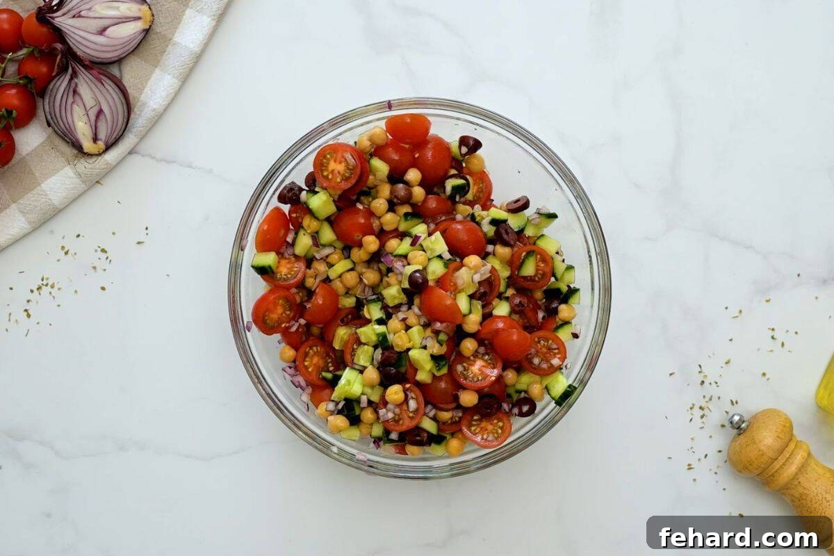 Mixing Chickpea Salad All the delicious ingredients for Mediterranean Chickpea Salad including chickpeas, cucumbers, olives, tomatoes, and red onions being tossed together in a large mixing bowl with dressing.