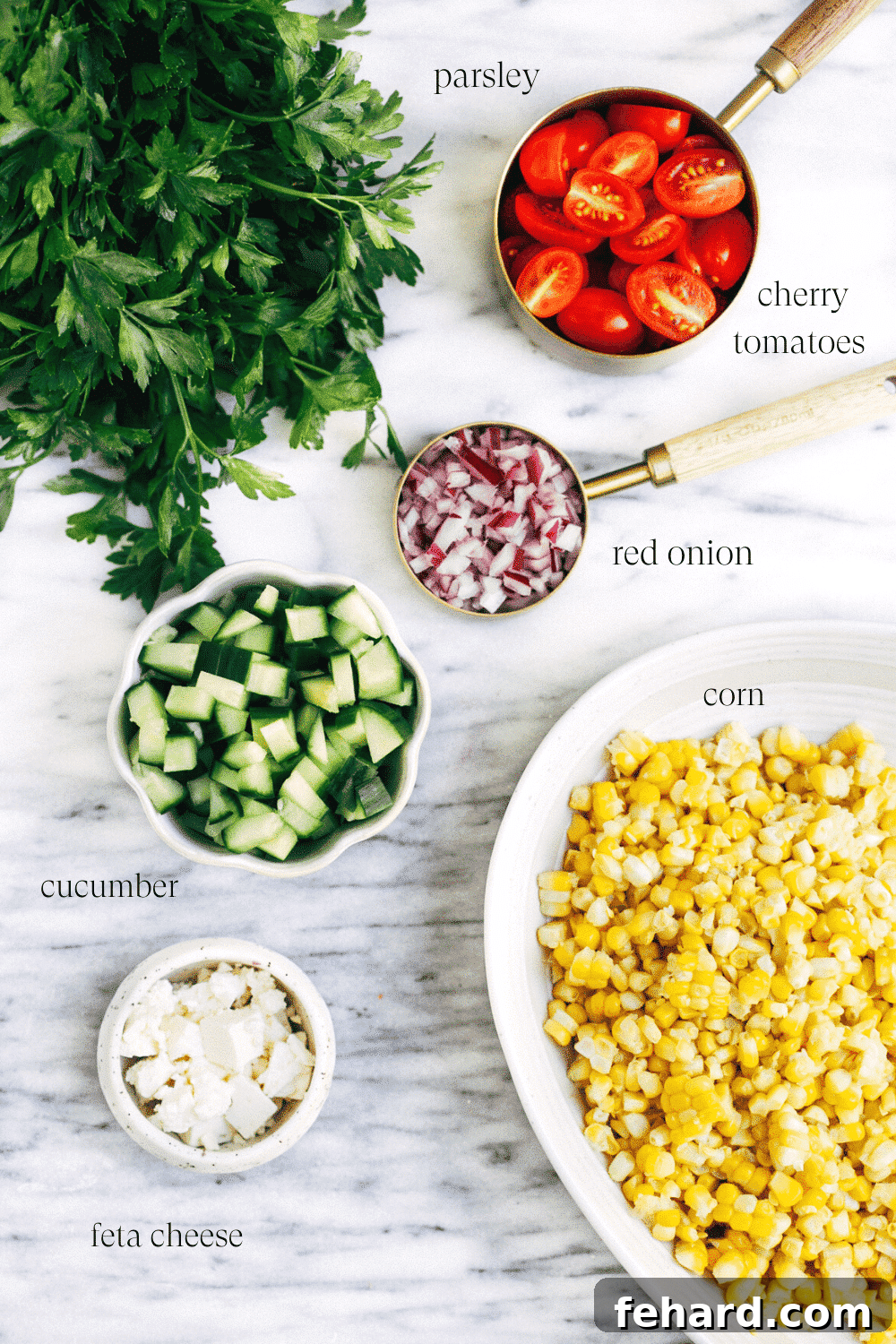 Zesty Corn Salad 3 Ingredients laid out on a marble board for making a fresh corn salad, including corn on the cob, cherry tomatoes, cucumber, red onion, and feta cheese.