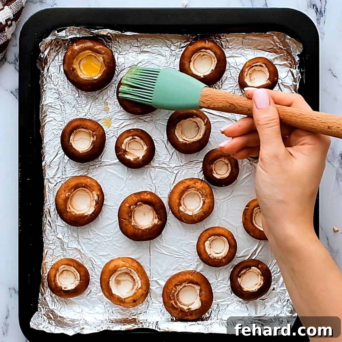 Easy Stuffed Mushroom Preparation Pastry brush applying melted butter to the inside of button mushroom caps on a baking sheet.