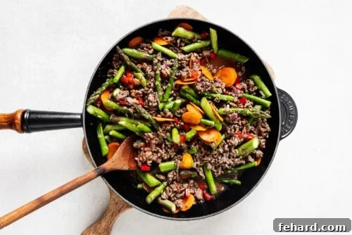 Ground beef and vegetables simmering in a skillet with the lid on, allowing flavors to meld.