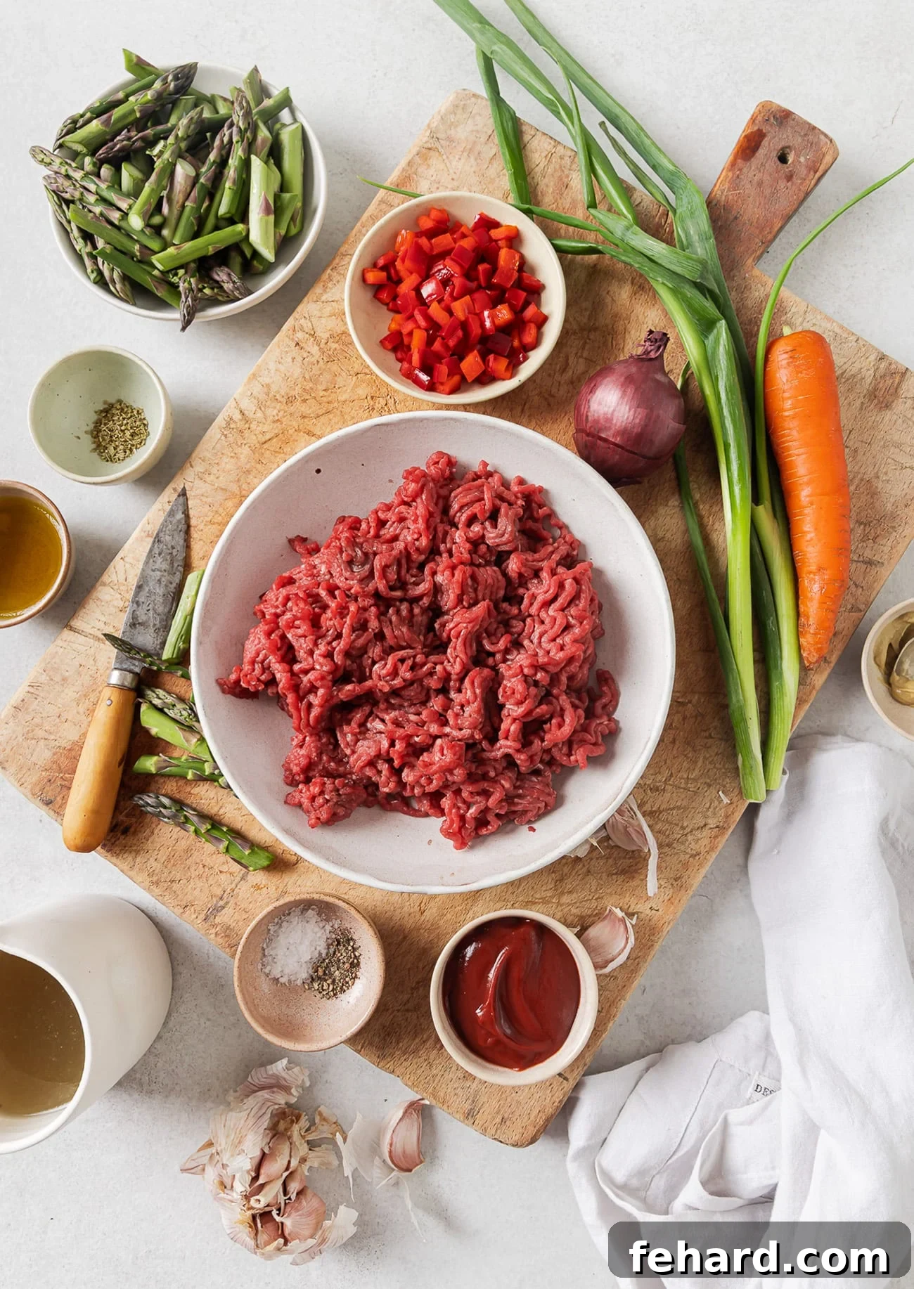 Assorted fresh ingredients for a ground beef and vegetable skillet, including ground beef, bell peppers, asparagus, carrots, and onions.