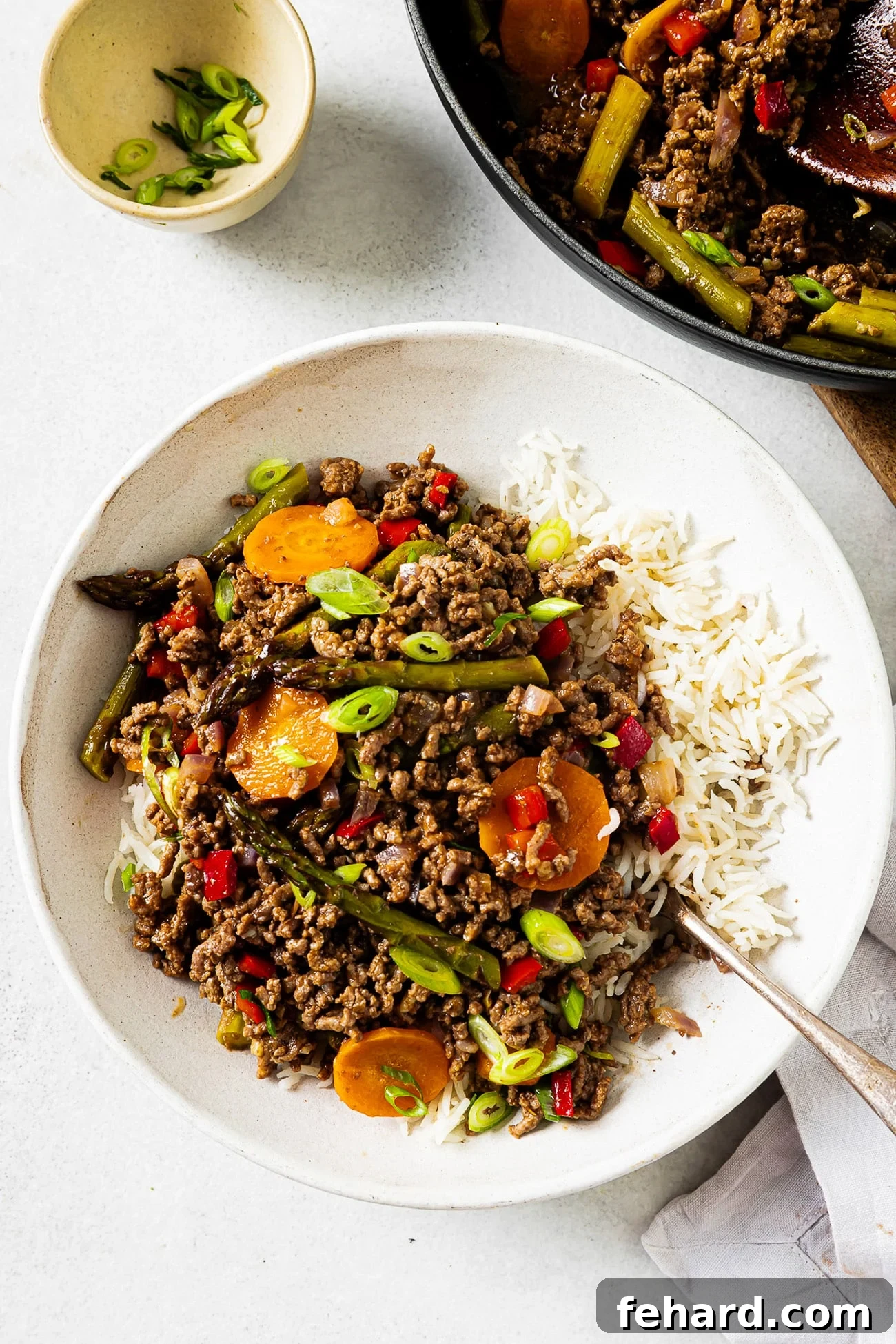Overhead view of ground beef with vegetables and rice served in a white bowl, garnished with green onions.
