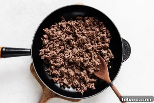 Ground beef browning in a skillet, creating a rich base for the dish.