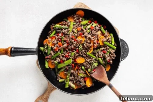 Ground beef and colorful vegetables like bell peppers, carrots, and asparagus sautéing in a skillet.