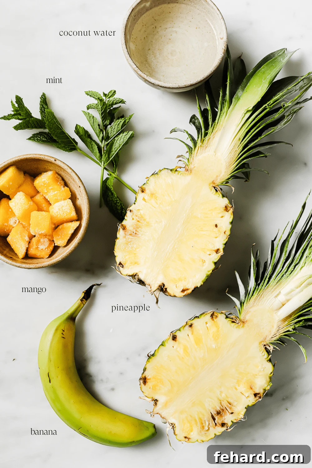 Pre-measured ingredients for a pineapple mango smoothie arranged on a white marble countertop.