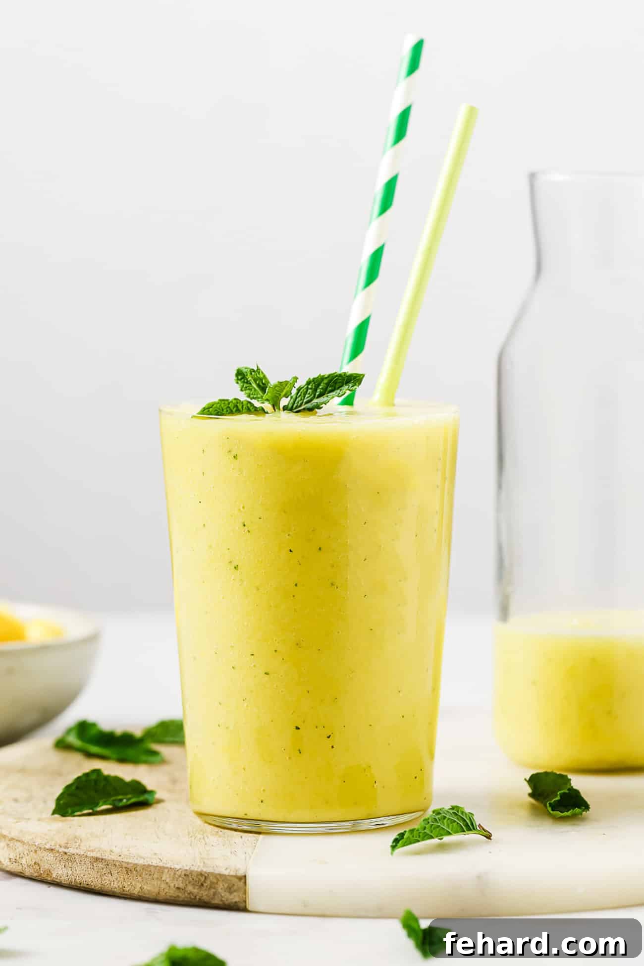 A tall glass of vibrant pineapple mango smoothie garnished with fresh mint on a summer day.