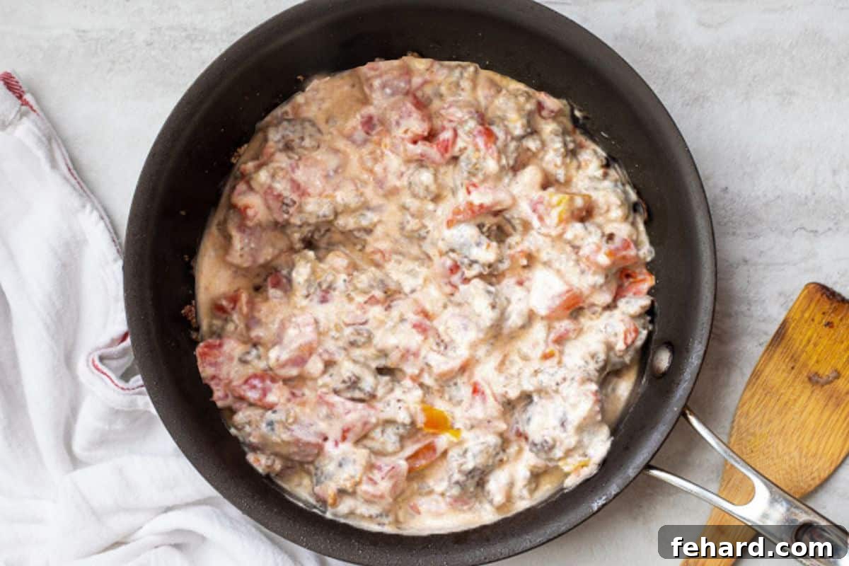 Cream cheese, Rotel tomatoes, and sausage simmering together in a sauté pan, melting into a creamy dip.
