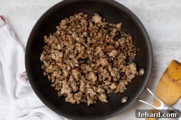 Browned sausage in skillet next to wooden spoon.