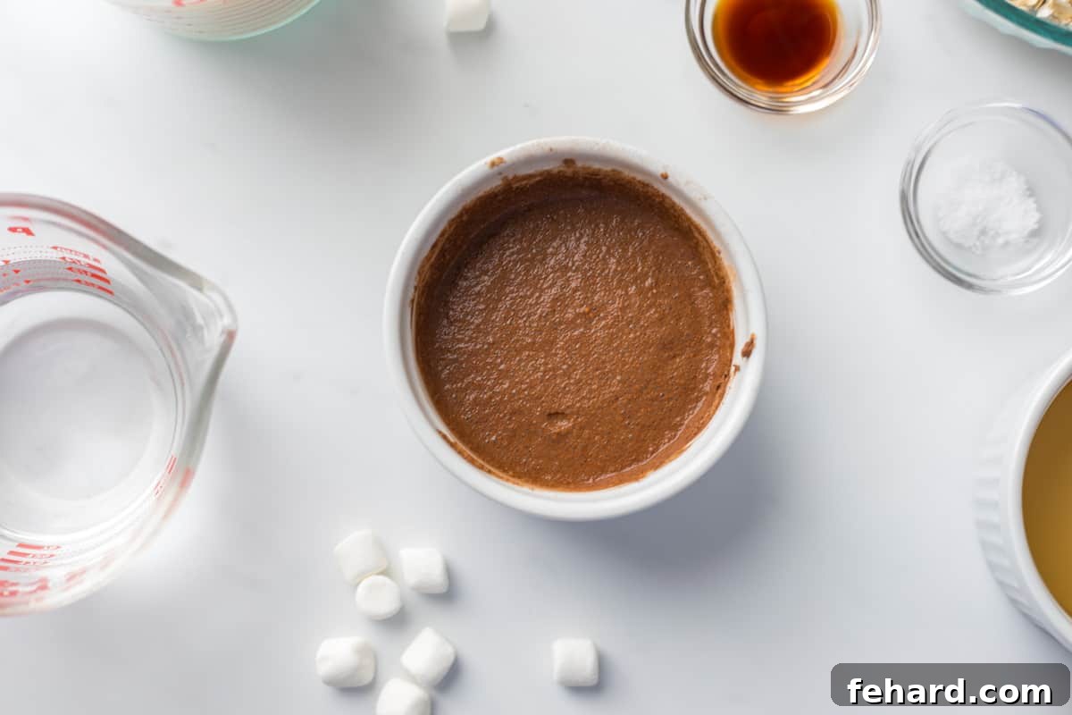 Cocoa powder whisked smoothly with water in a small bowl, next to other hot chocolate oatmeal ingredients.