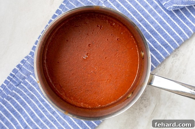 A saucepan filled with rich, simmering red enchilada sauce, ready for serving.