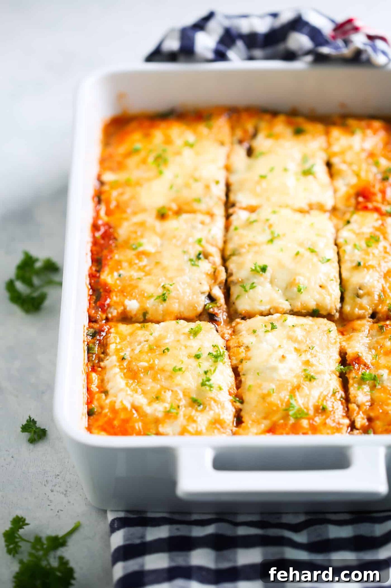 A large, perfectly baked eggplant lasagna sits in a white baking dish, its top golden and bubbly, ready to be served.