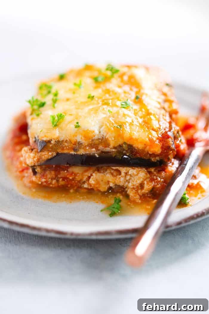 A perfectly portioned slice of golden-brown eggplant lasagna, revealing its delicious layers of cheese and sauce, served on a pristine white plate.