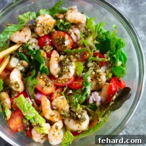 Glass bowl containing pesto shrimp tomato salad.
