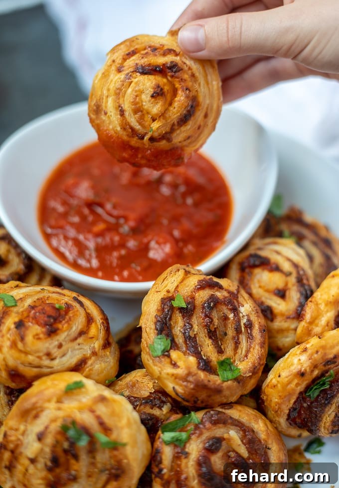 Pizza Rolls Pizza roll being dipped in marinara sauce. A golden-brown, flaky pizza roll is held above a small white bowl of rich red marinara sauce, ready for dipping.