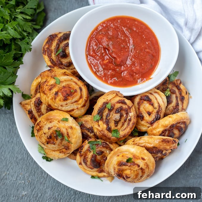 Pizza Roll Ups made with puff pastry Platter of pizza rolls with bowl of marinara sauce. A beautifully arranged platter showcases numerous golden-brown pizza roll-ups, with a central bowl of marinara for dipping.