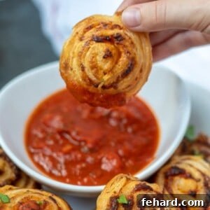 Pizza Roll-Up being held above pizza sauce for dipping. A single, perfectly baked pizza roll-up is shown, ready to be dipped into a bowl of pizza sauce.