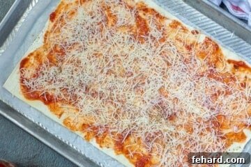 Thin layer of pizza sauce and cheese on puff pastry. The puff pastry is spread with sauce and cheese, ready for rolling.