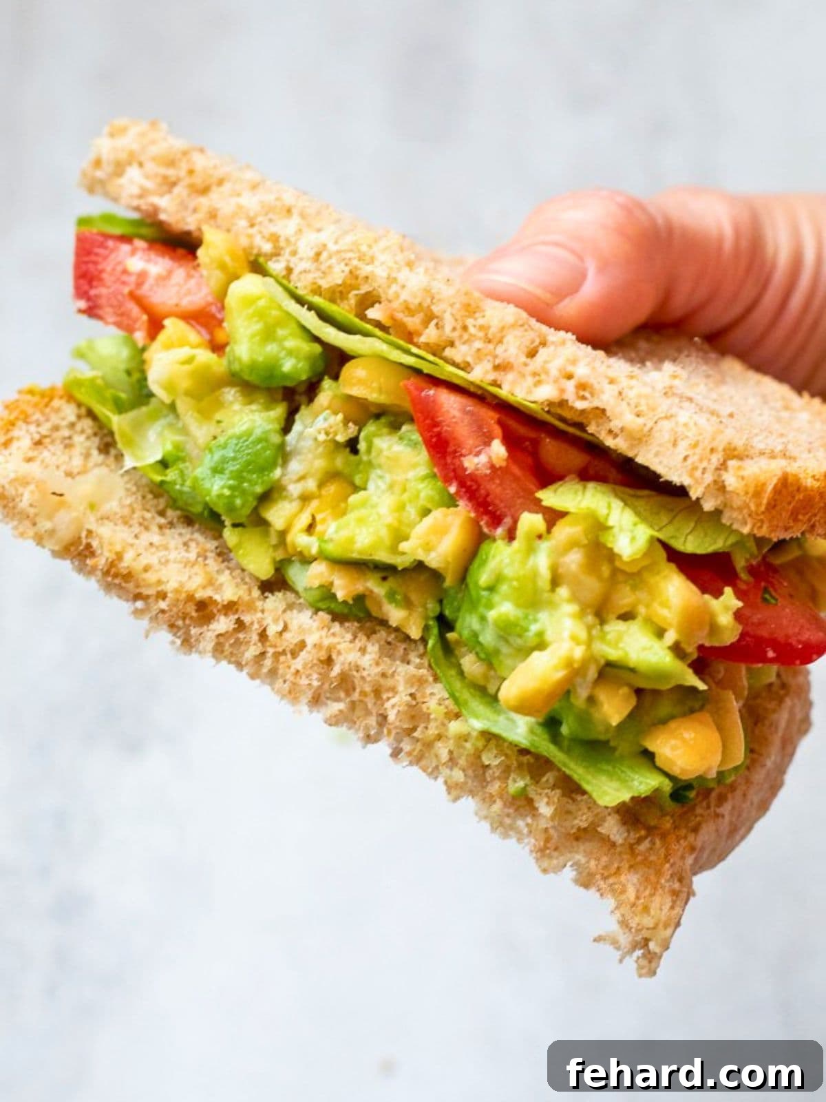 Creamy Chickpea Avocado Salad Sandwich Chickpea Avocado Salad on wheat bread topped with fresh tomatoes and crisp lettuce, showcasing a perfect vegan sandwich.