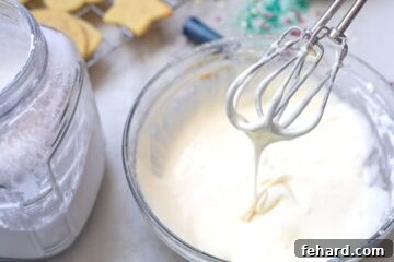 Creamy Sugar Cookie Frosting dripping off mixer beaters into a glass bowl, illustrating ideal consistency.