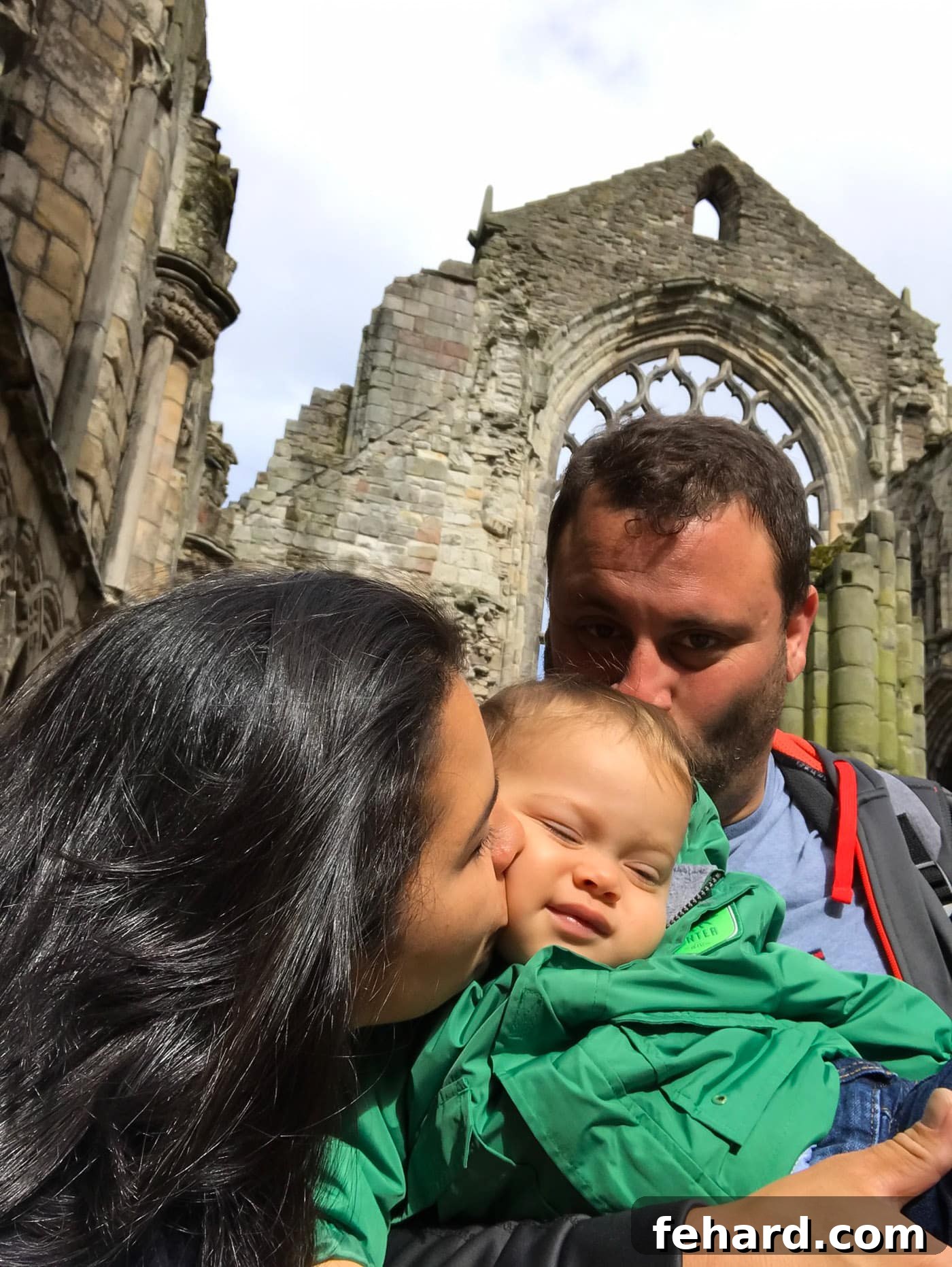 Parents sharing a tender moment, kissing their toddler on the head and cheek