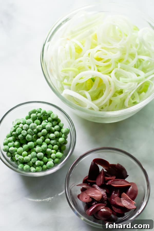 Preparation bowls neatly display sliced leeks, vibrant green frozen peas, and glistening Kalamata olives, ready for cooking.