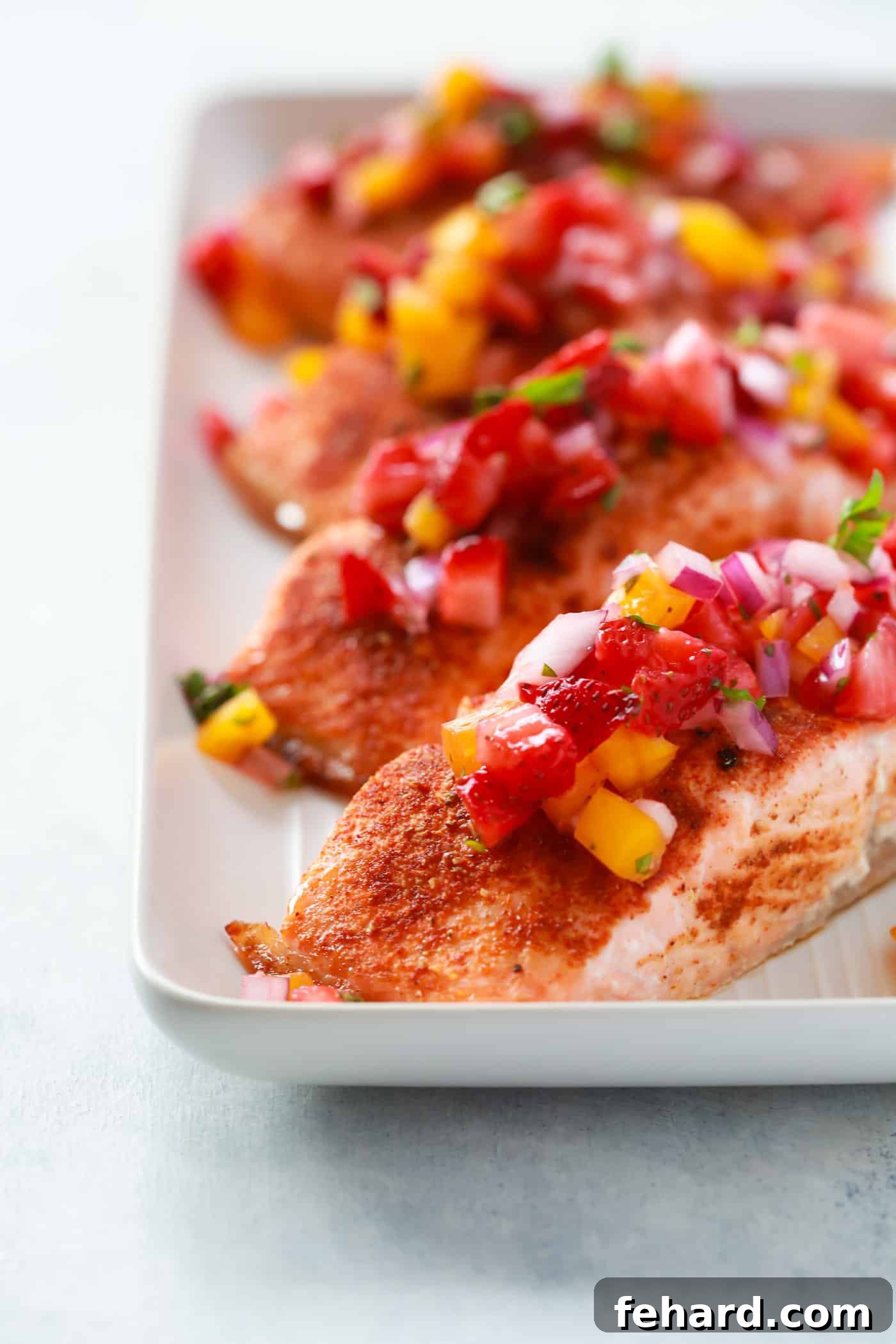 Flaky Cajun-spiced salmon fillets topped with bright, fresh strawberry salsa, presented on a plate for a healthy summer meal.