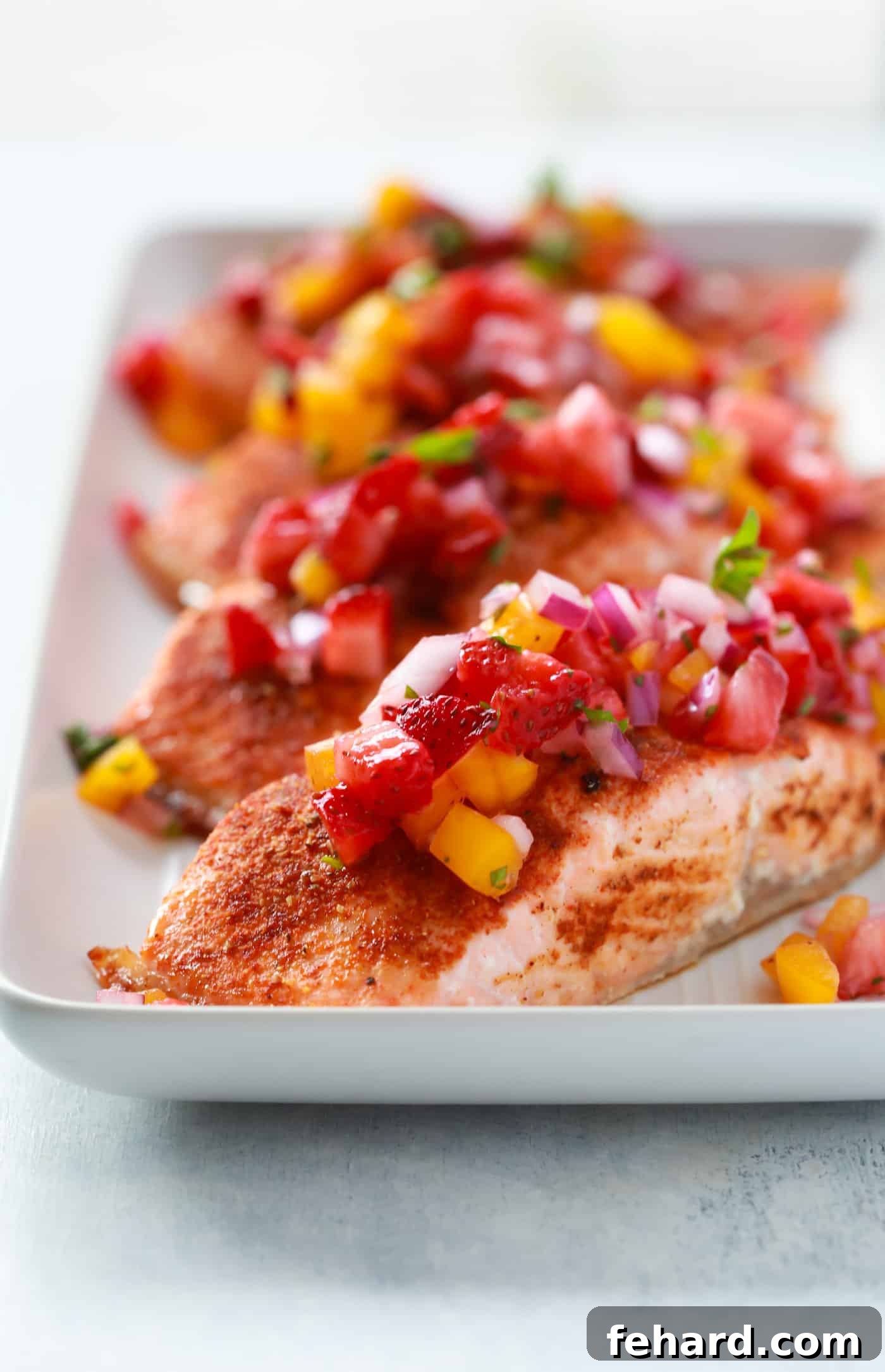 Close-up view of four salmon fillets seasoned with Cajun spices on a parchment-lined baking sheet, ready for the oven.