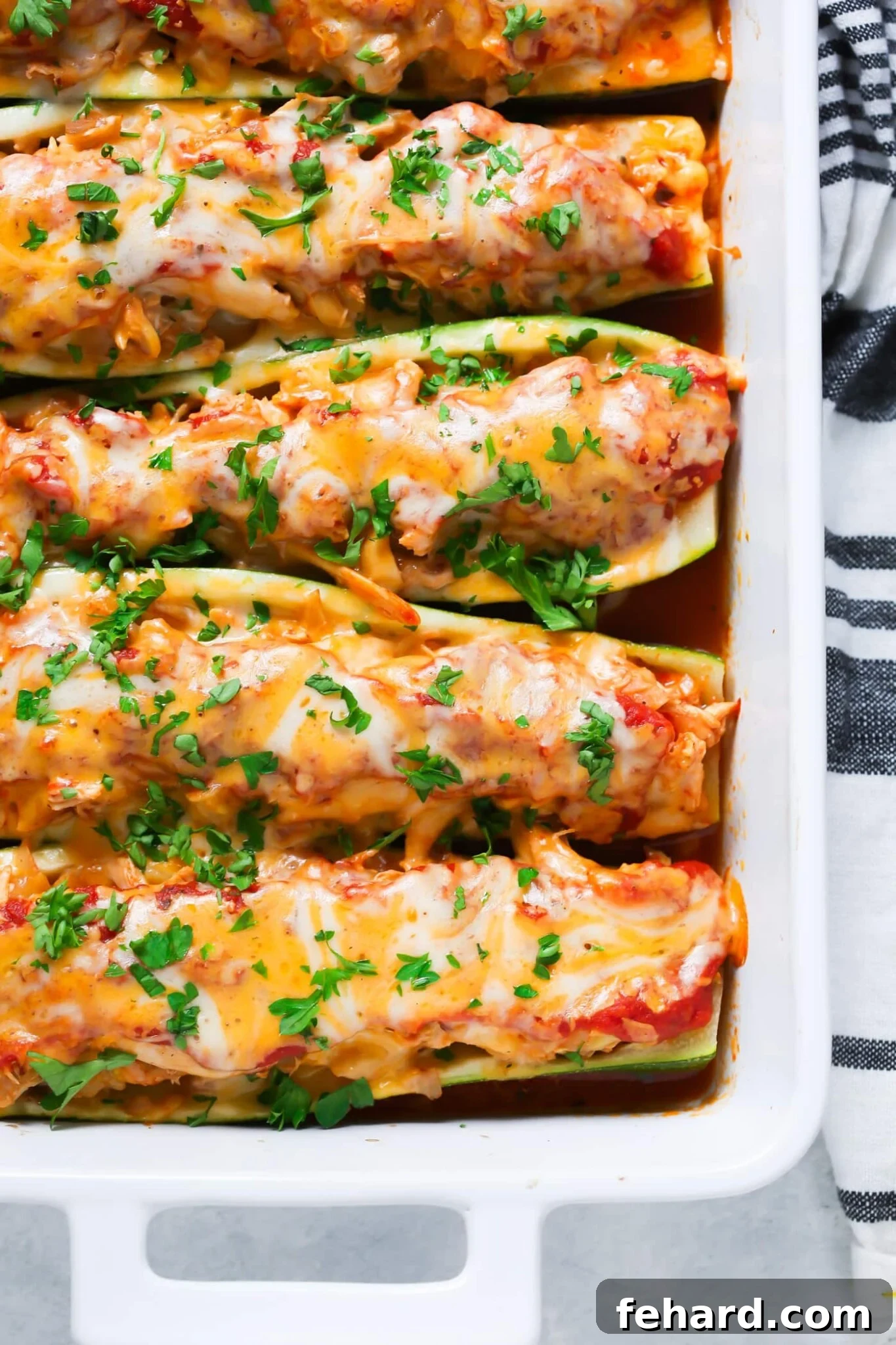 Try this low-carb and gluten-free 5-Ingredient Chicken Zucchini Boats that are stuffed with chicken, homemade tomato pasta sauce and mozzarella/ cheddar cheese. overhead view of 5-Ingredient Chicken Zucchini Boats in a white casserole