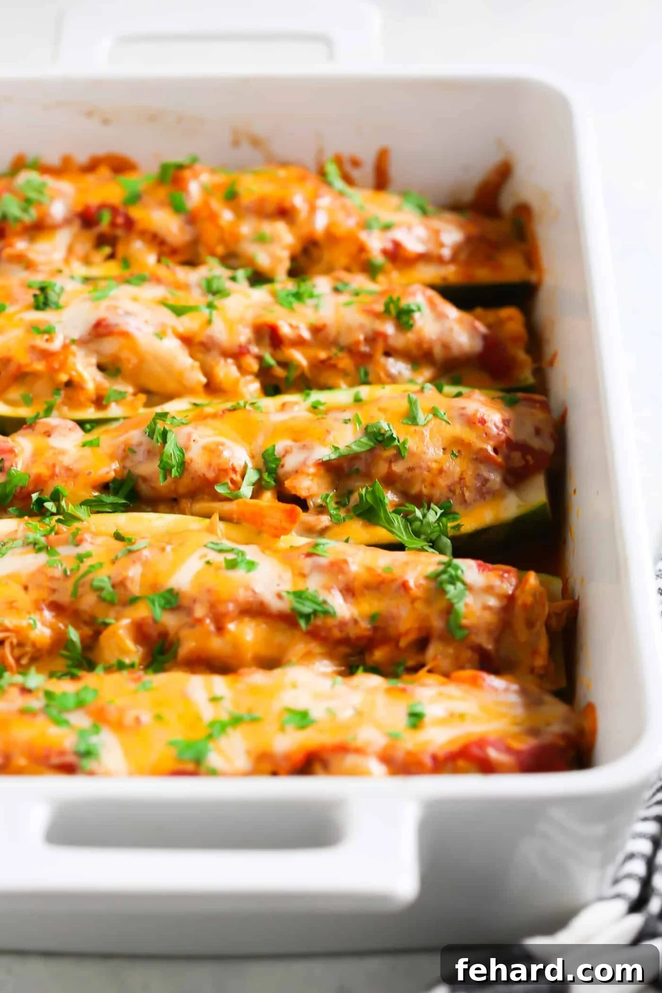 Try this low-carb and gluten-free 5-Ingredient Chicken Zucchini Boats that are stuffed with chicken, homemade tomato pasta sauce and mozzarella/ cheddar cheese. overhead view of 5-Ingredient Chicken Zucchini Boats in a white casserole