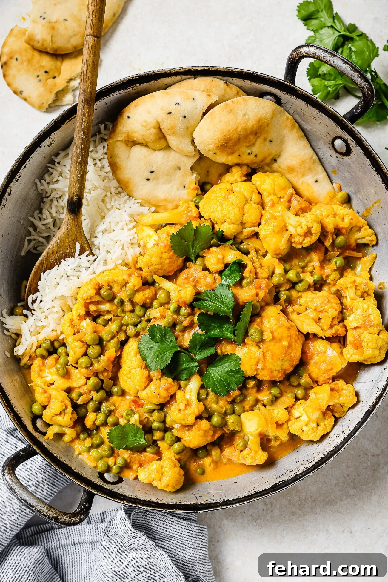 An overhead view of cauliflower curry over rice with a side of naan.