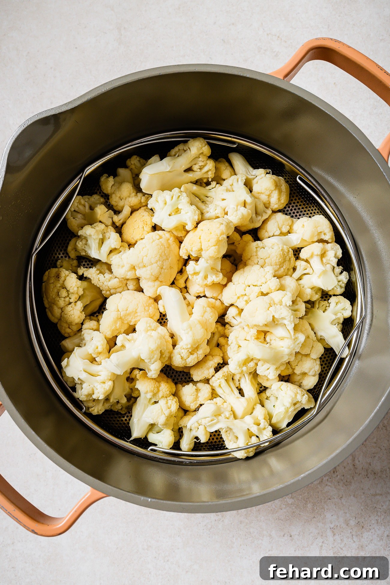 Cauliflower florets in a steamer basket inside of a large pot.