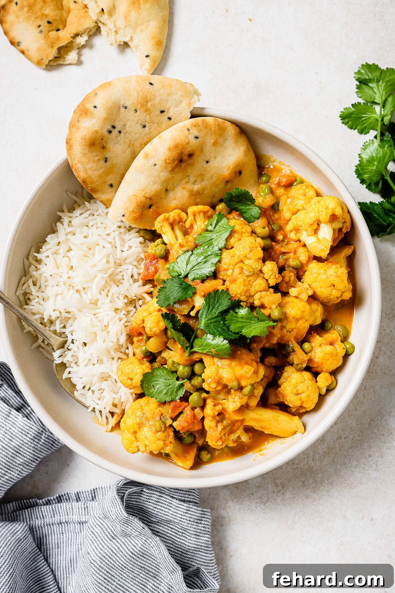 Cauliflower curry in a bowl with rice and a side of naan.