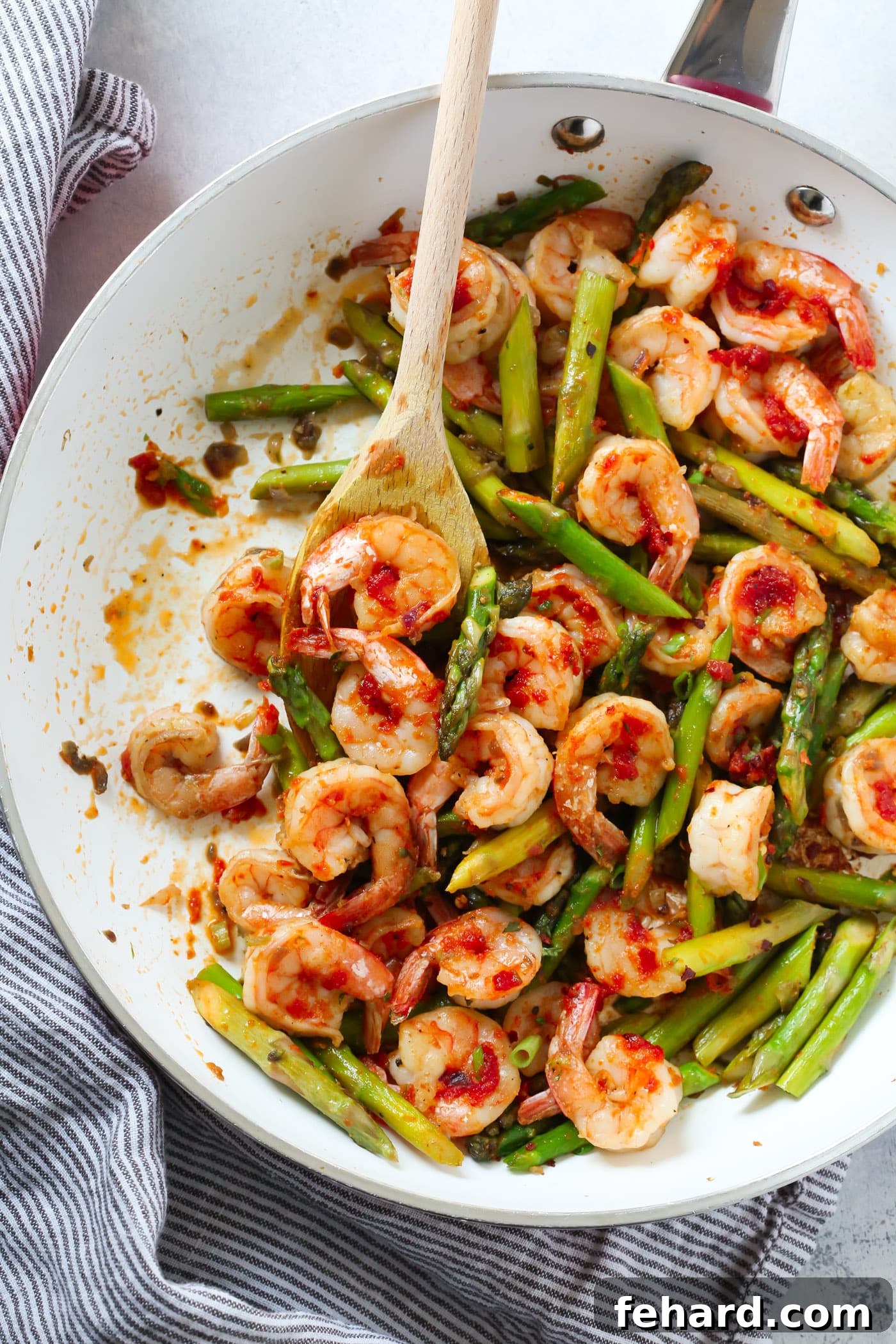 Fresh shrimp and vibrant green asparagus cooking together in a skillet, coated in a luscious sun-dried tomato pesto, promising a quick and healthy meal.