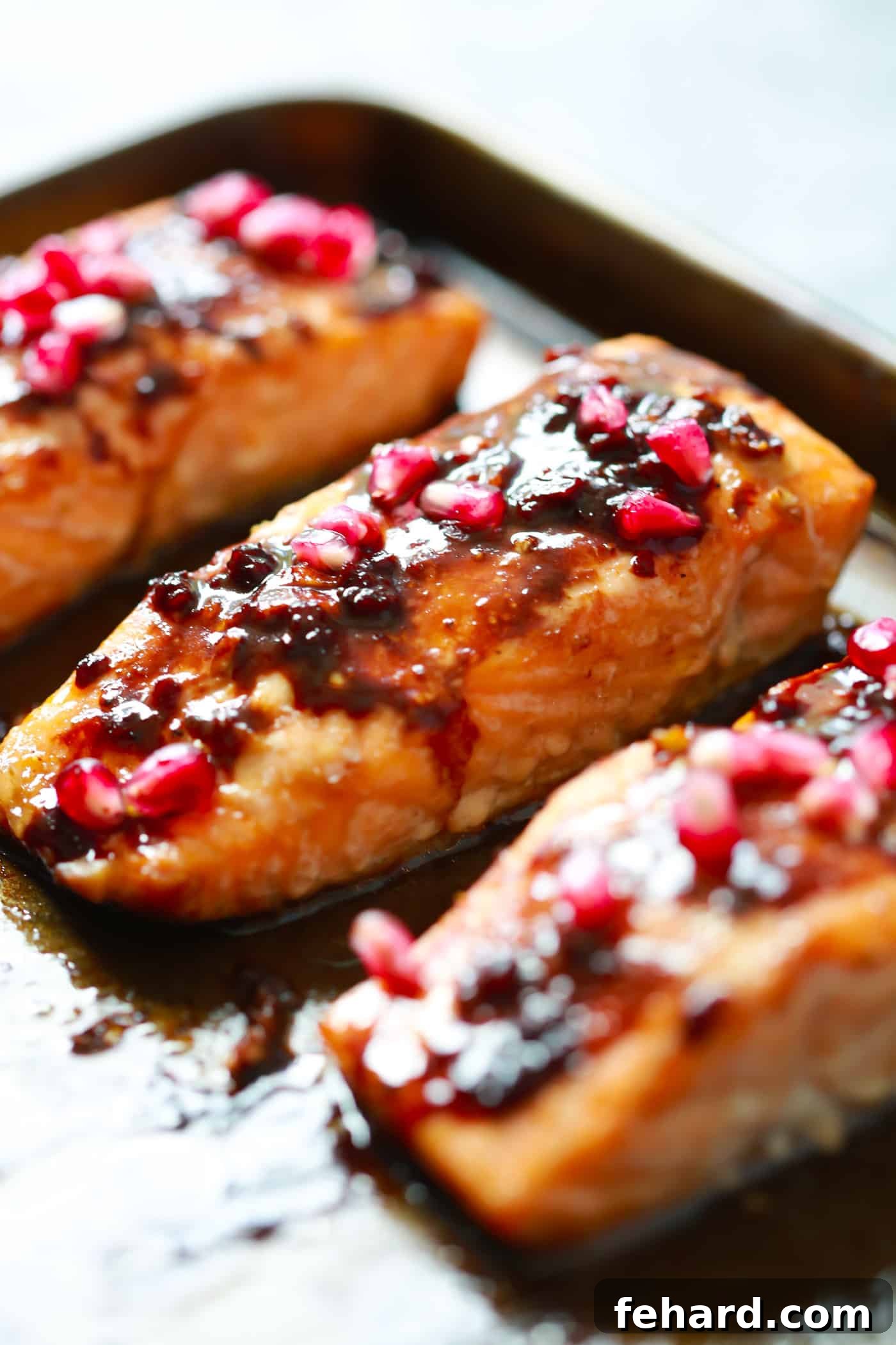 Baked Pomegranate Glazed Salmon with a healthy, sugar-free tangy glaze. Close-up of three beautifully cooked salmon fillets on a parchment-lined baking sheet, glistening with glaze.