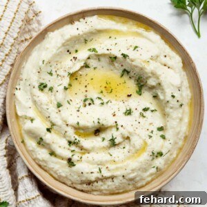 A top-down view of creamy mashed cauliflower in a bowl, with a spoon digging in.