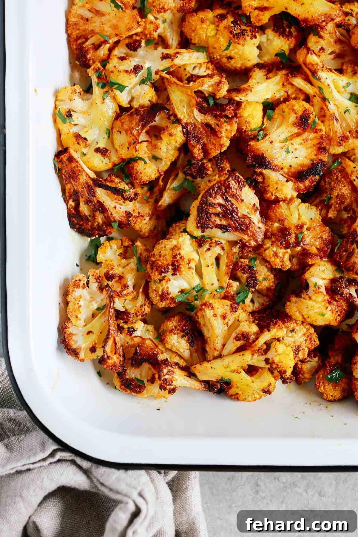 Closeup of perfectly roasted cauliflower florets in a white baking sheet, seasoned with spices and slightly browned