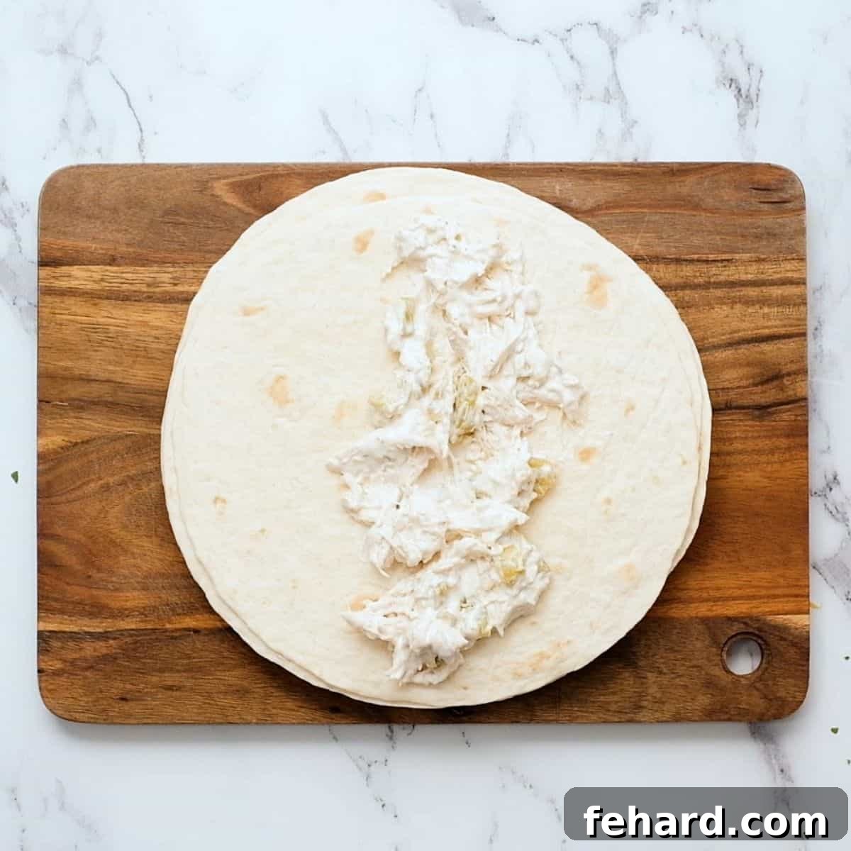 How to Fill Chicken Enchiladas Shredded chicken and cream cheese filling spread down the center of a soft flour tortilla, ready to be rolled.