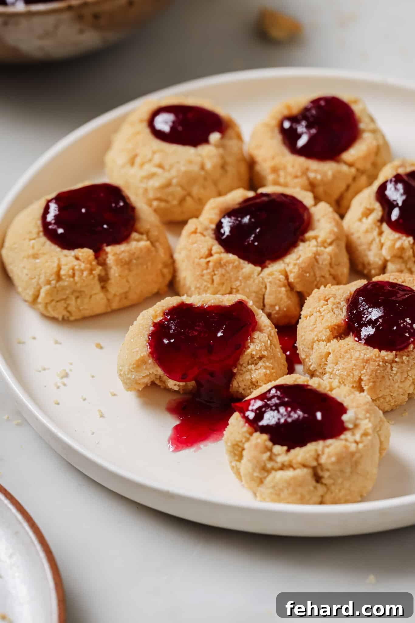 Closeup view of a single Cranberry Thumbprint Cookie on a white plate, highlighting its texture and filling.