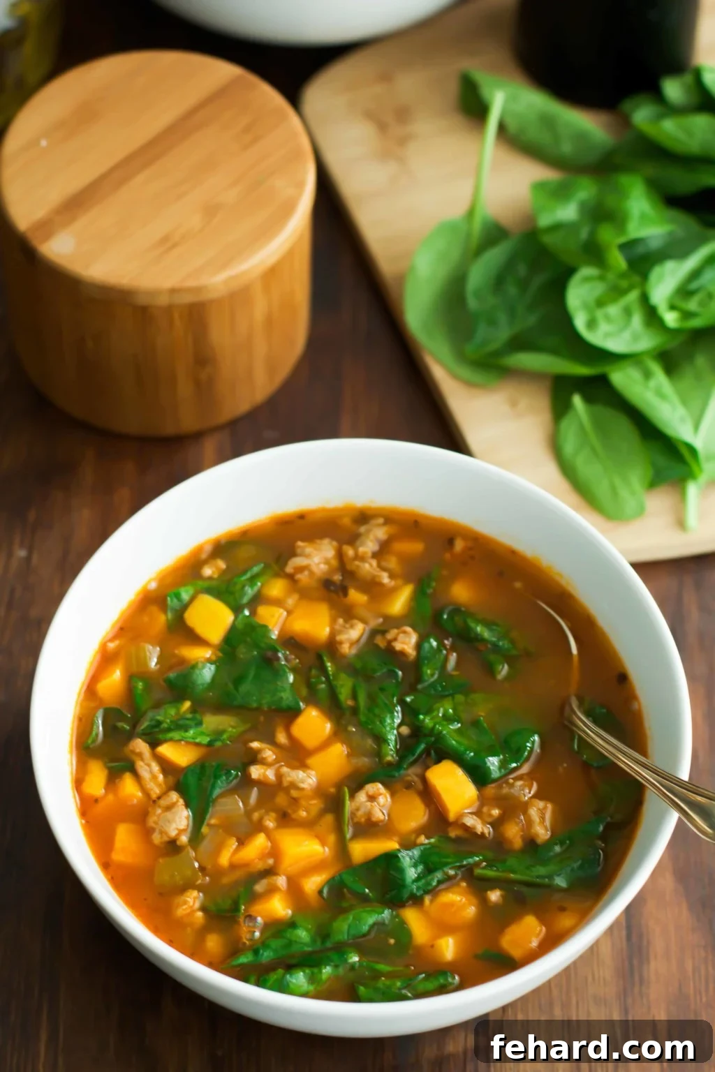 Spinach Sweet Potato Soup Close-up A white ceramic bowl filled with vibrant Spinach Sweet Potato Soup, with a spoon resting inside, showcasing the rich texture and colorful ingredients.