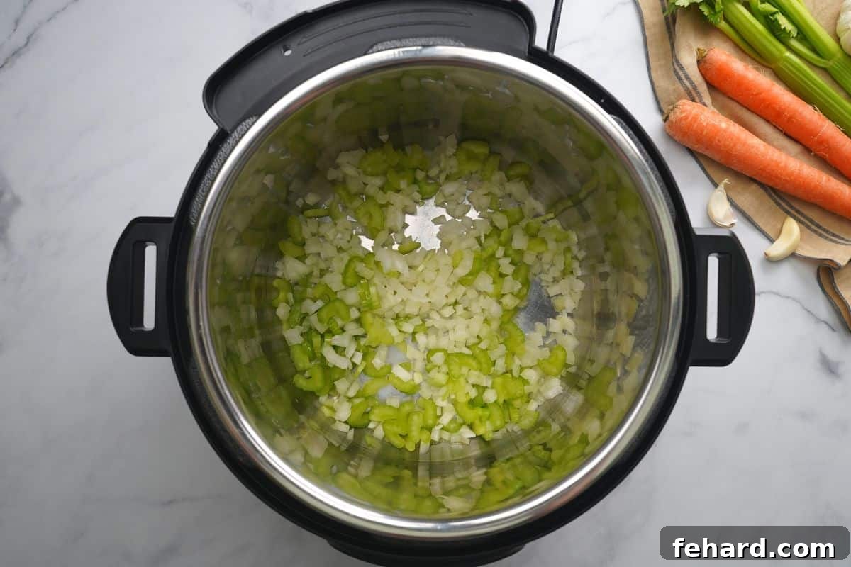 Minced celery and onions actively sautéing in the inner pot of an Instant Pot.