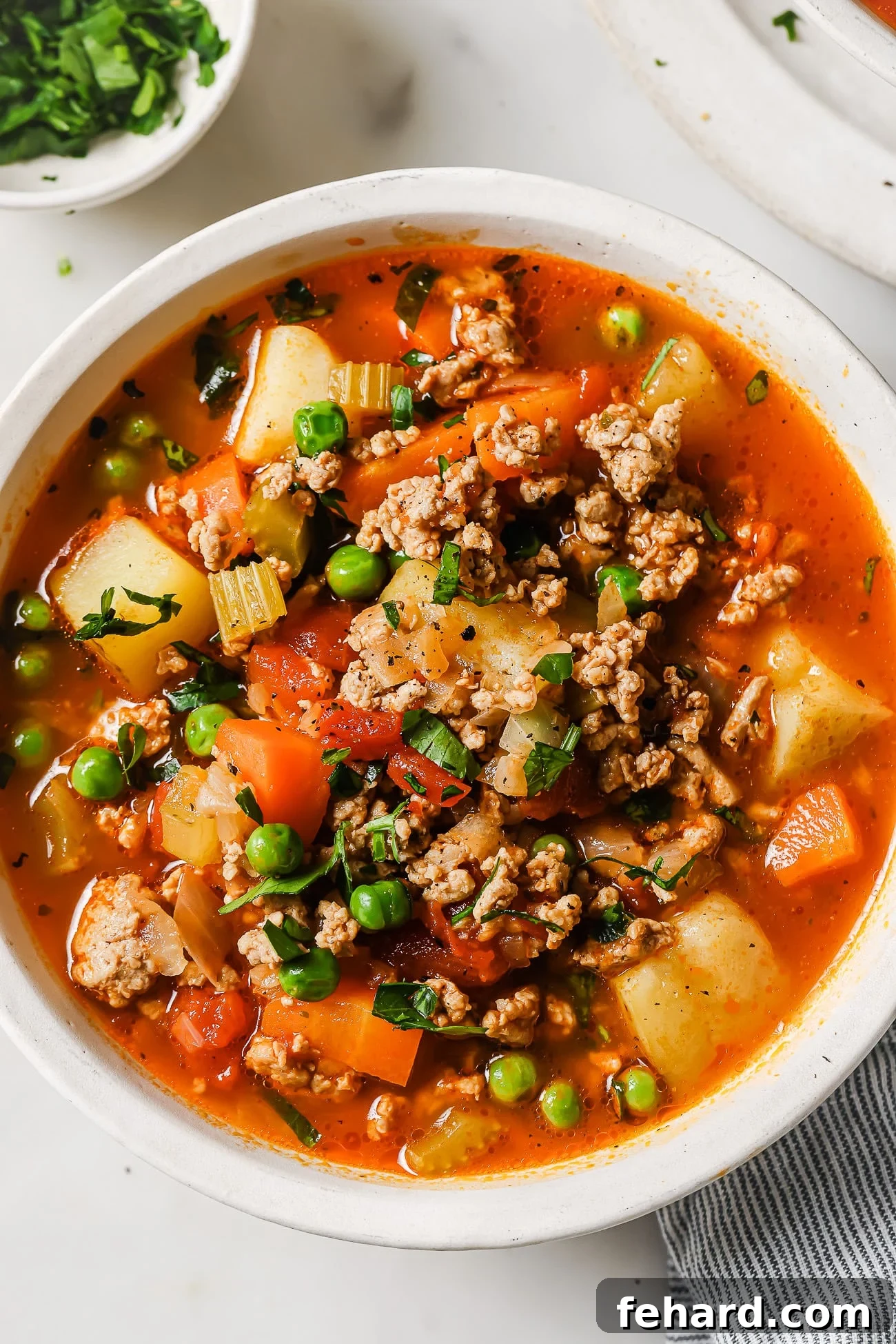 A close-up shot of the delicious ground turkey soup, garnished with fresh green herbs, in a white bowl.