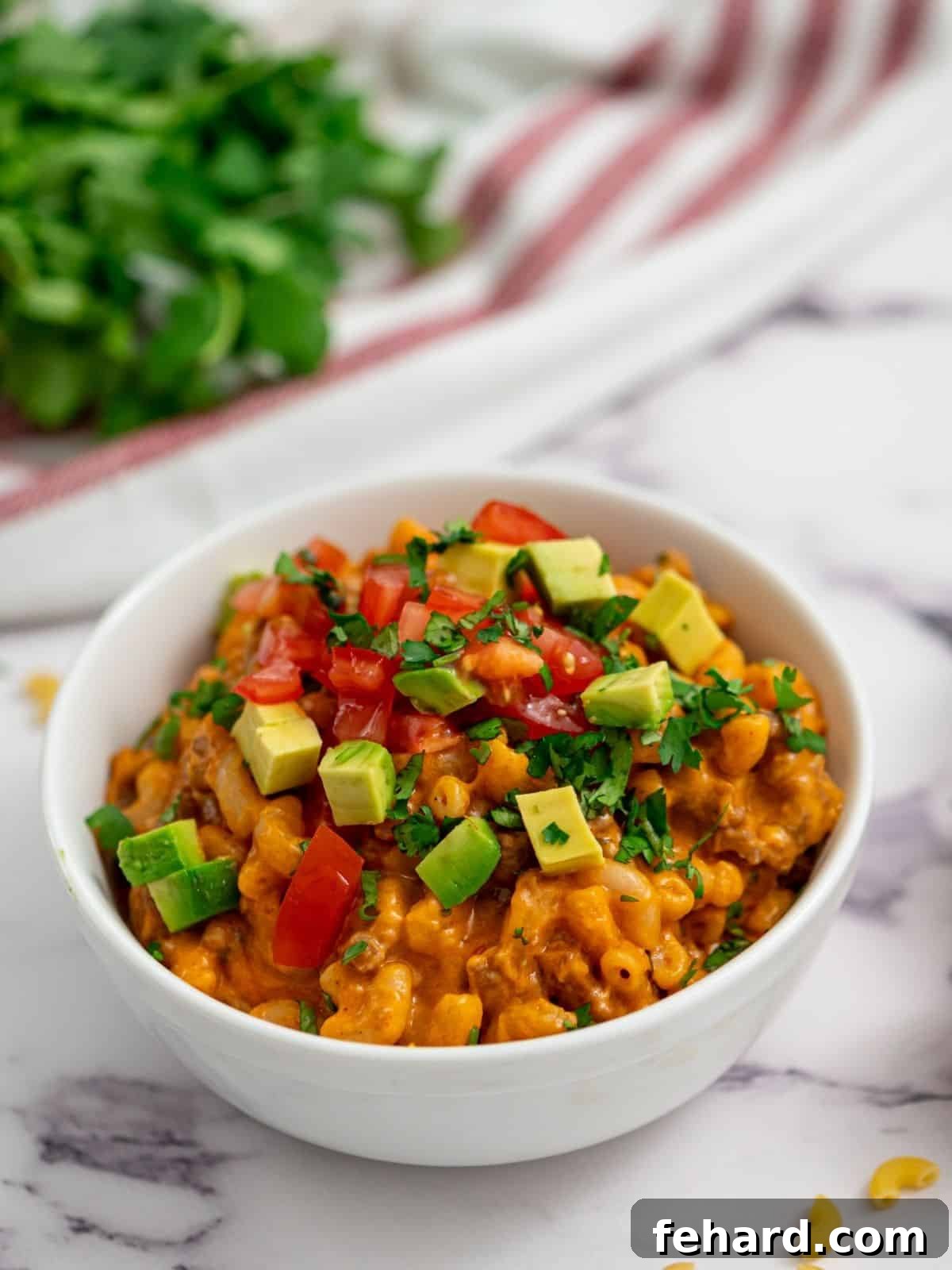 A delicious bowl of creamy Taco Pasta, generously topped with fresh diced tomatoes and creamy avocado slices, ready to be enjoyed.