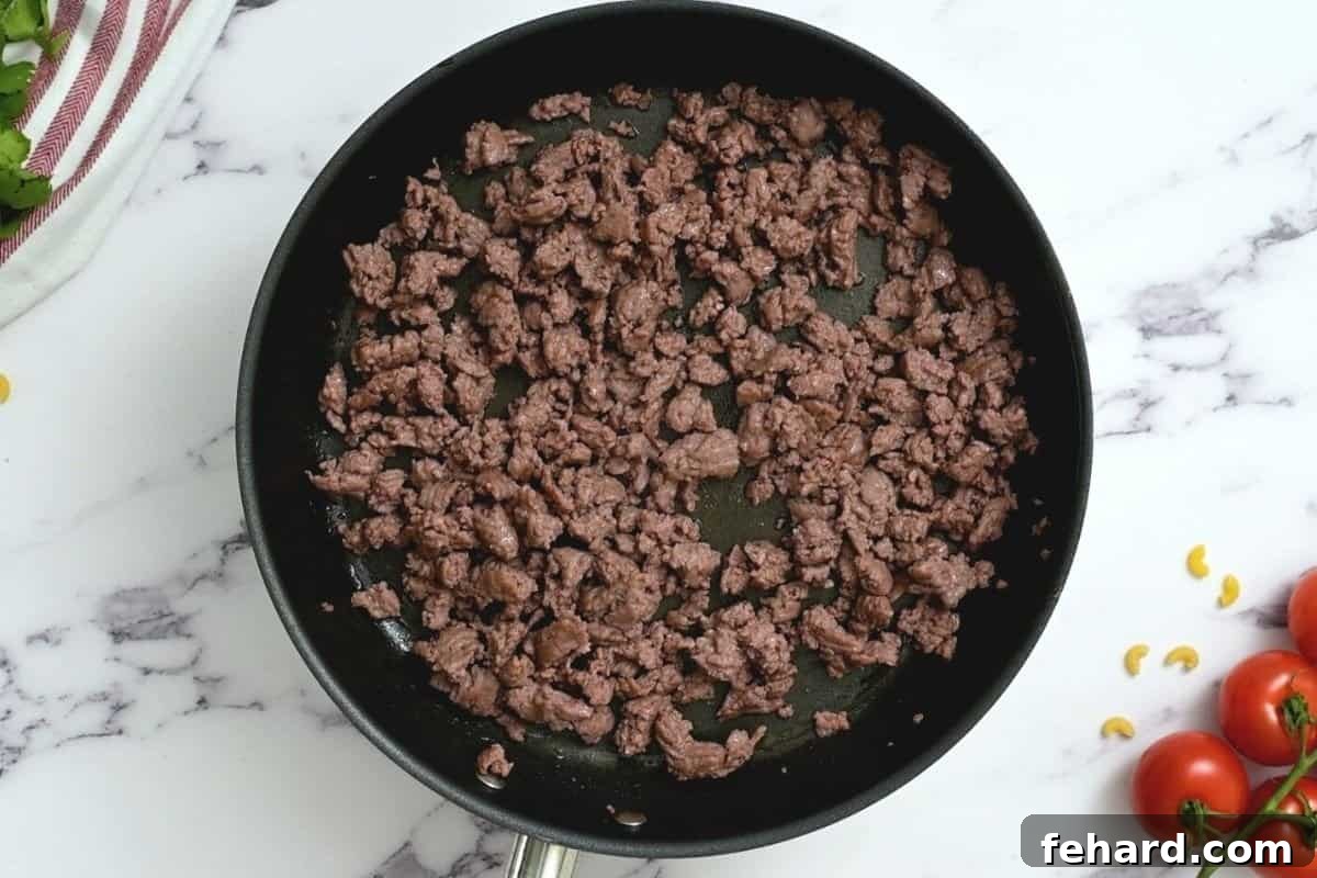 Ground beef is being expertly browned in a large skillet, ready for the next steps of the taco pasta recipe.