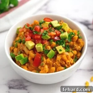 Bowl of creamy, cheesy taco pasta in white bowl topped with avocado and fresh herbs.