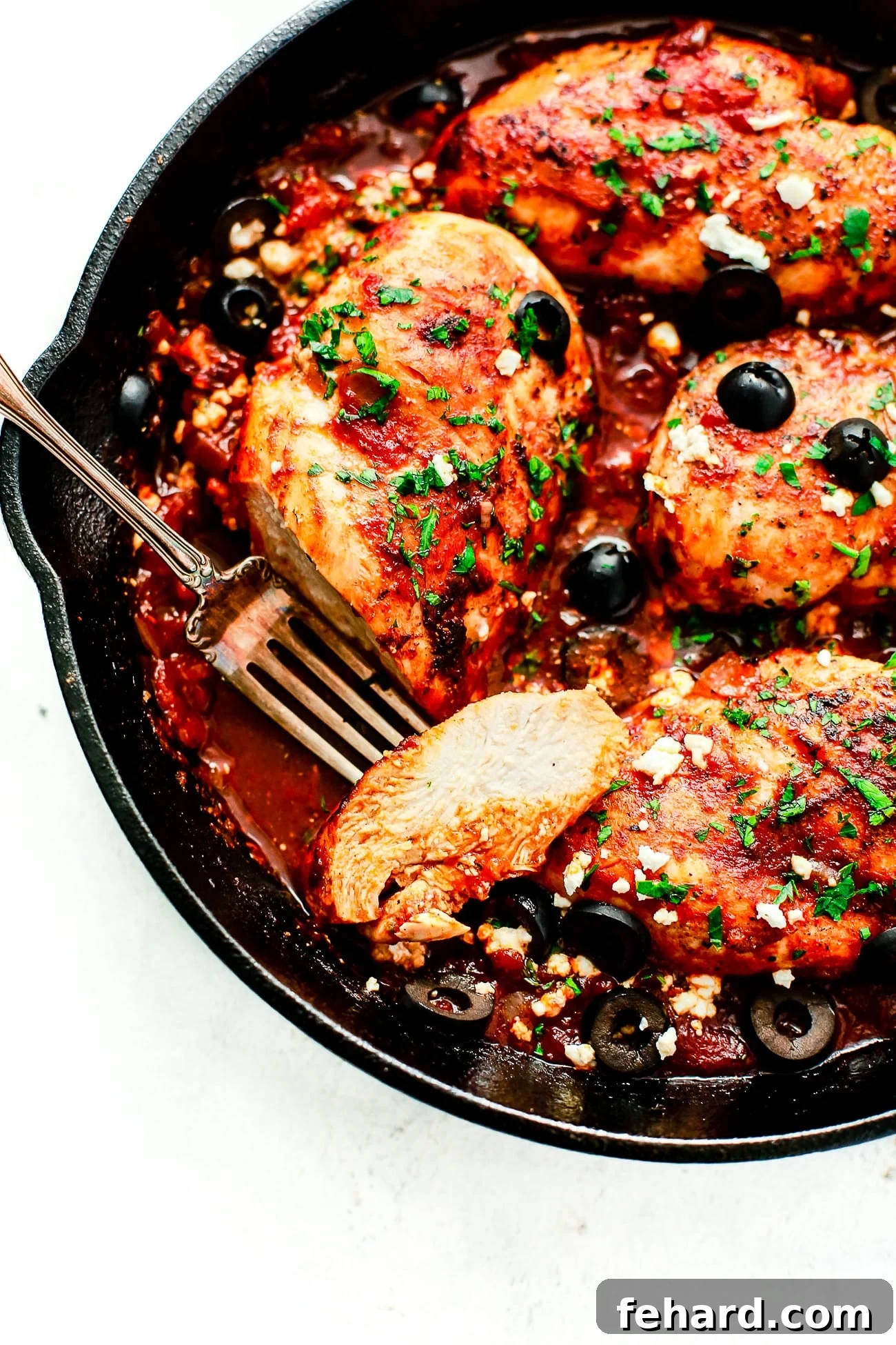 closeup view of a cast iron skillet containing Mediterranean Chicken breast, garnished with olives and feta