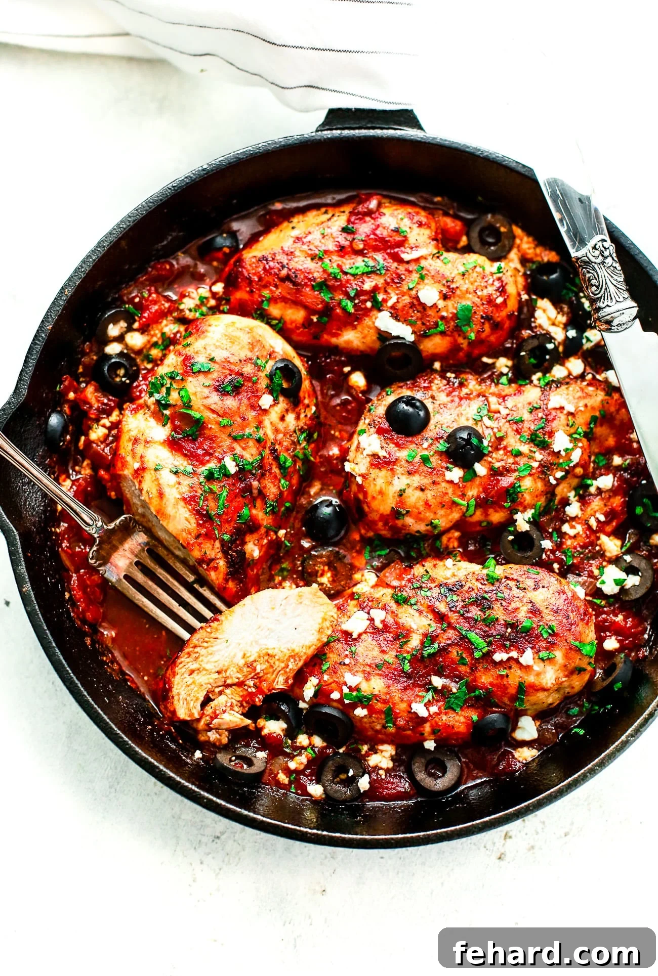 overhead view of a cast iron skillet containing Mediterranean Chicken breast garnished with olives and feta